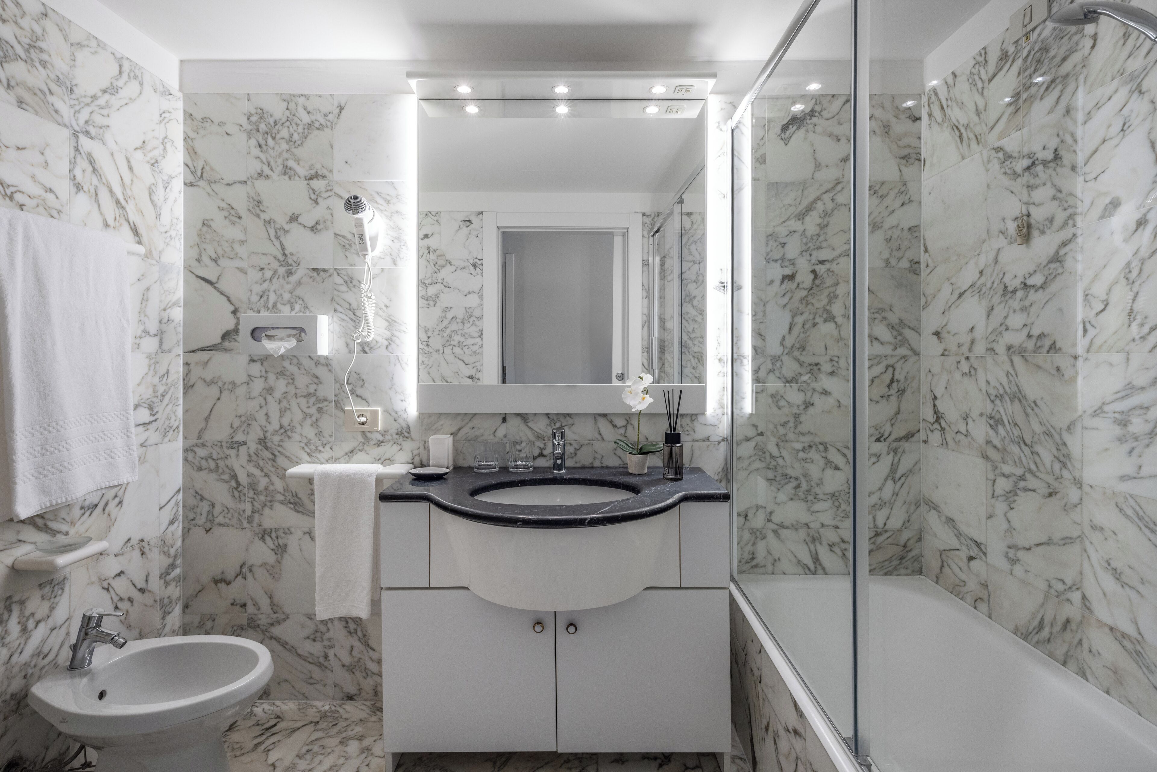 A bathroom with a marble sink, a glass-enclosed shower, and a white pedestal sink.