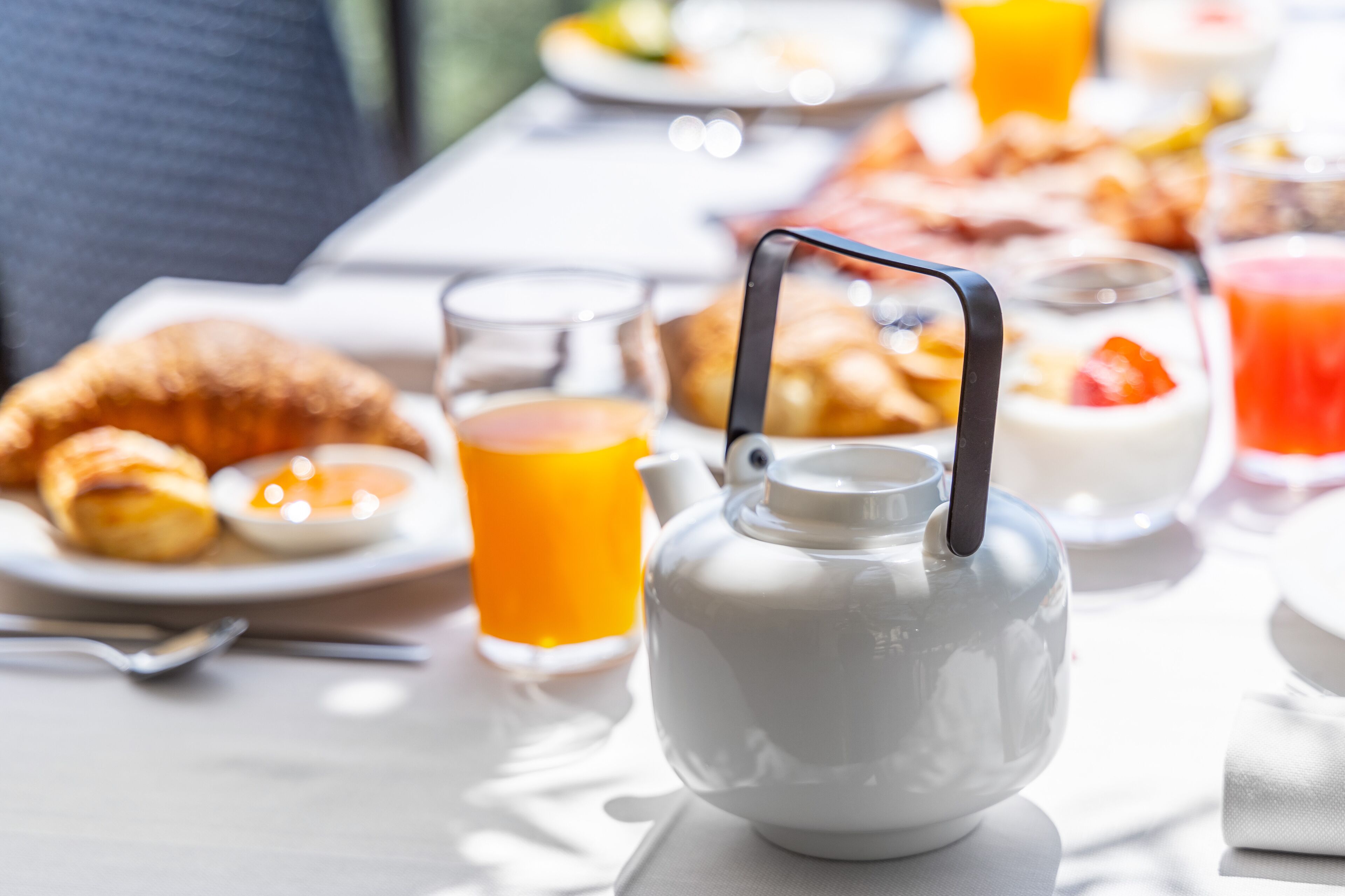 Ein Frühstückstisch mit Croissants, Orangensaft und einer Teekanne.