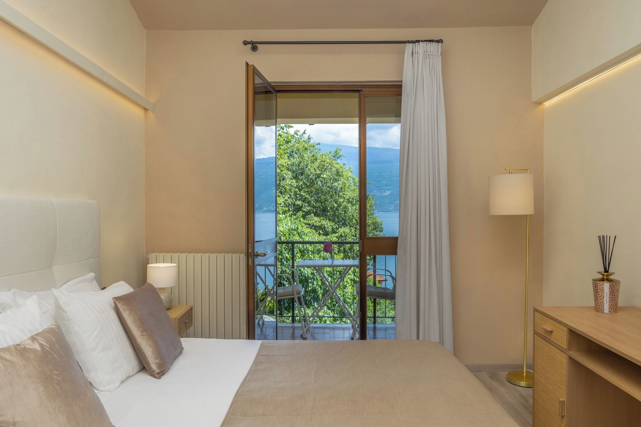 Una camera da letto con un letto, un comodino, una lampada, una scrivania e vista sul verde attraverso una finestra.