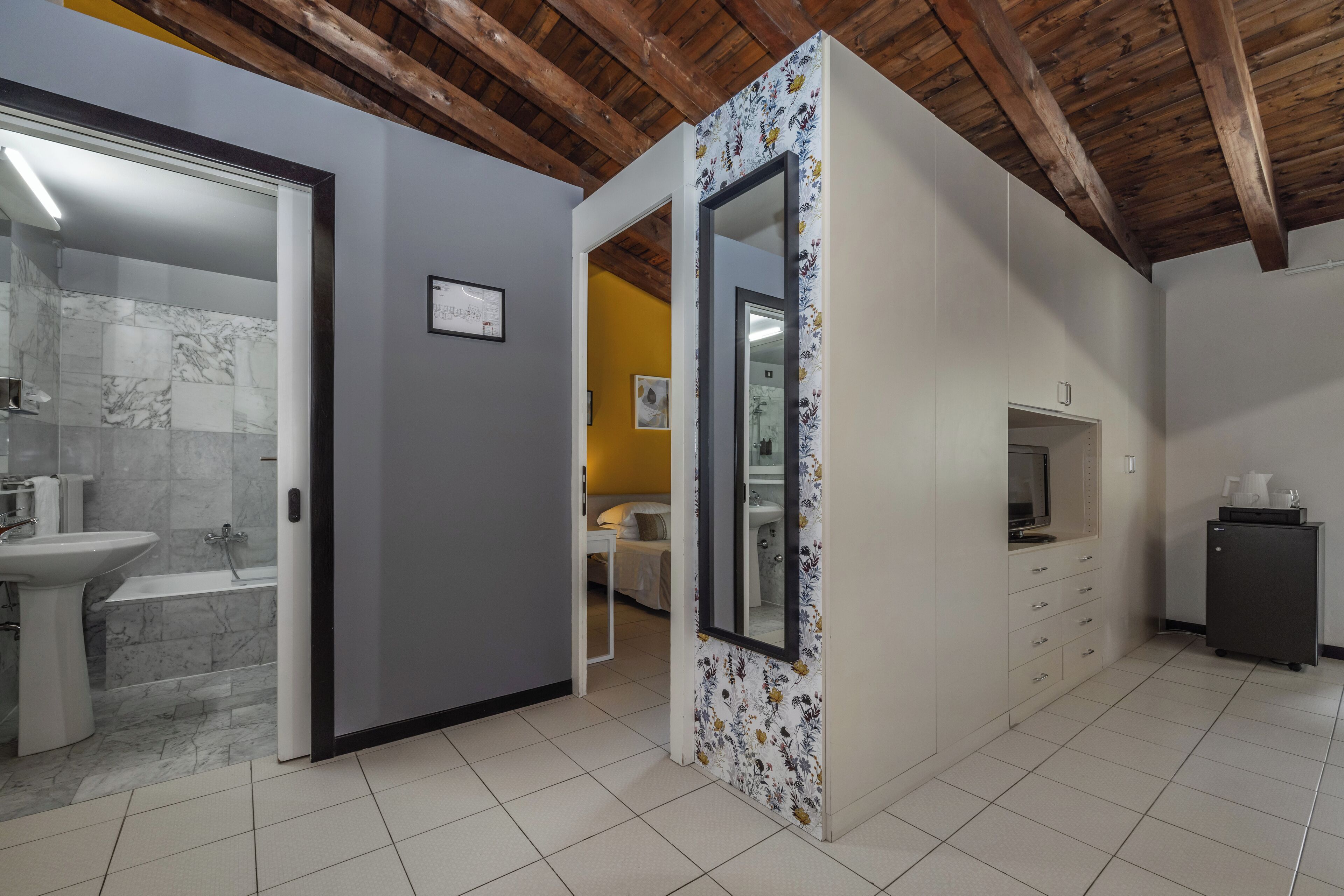 A modern bathroom with a marble sink, a bathtub, and a shower. There is a door leading to a bedroom with a bed and a bedside table.