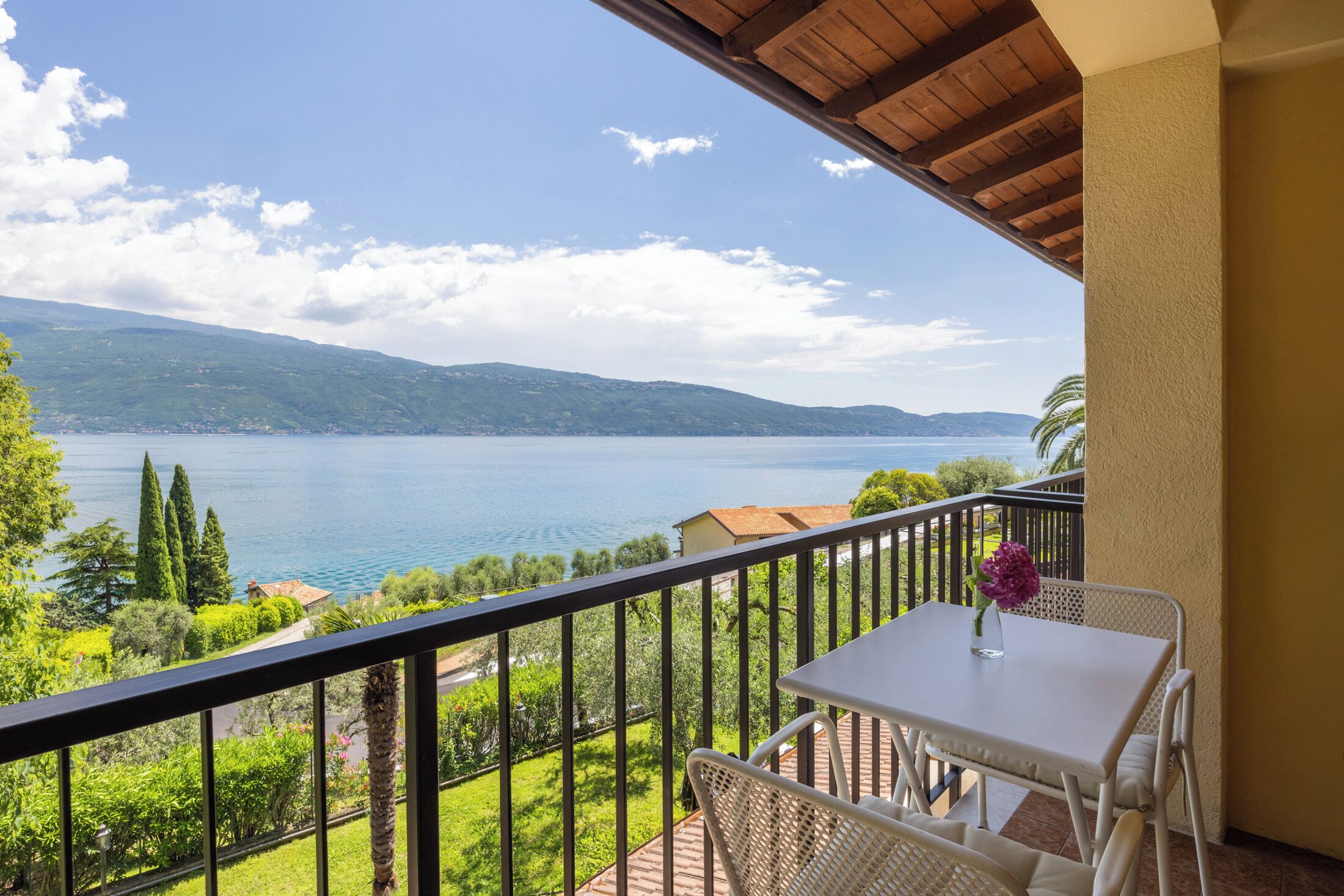 A balcony with a table and chairs, overlooking a lake with mountains in the distance.
