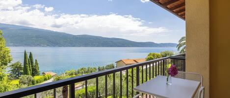 A balcony with a table and chairs, overlooking a lake with mountains in the distance.