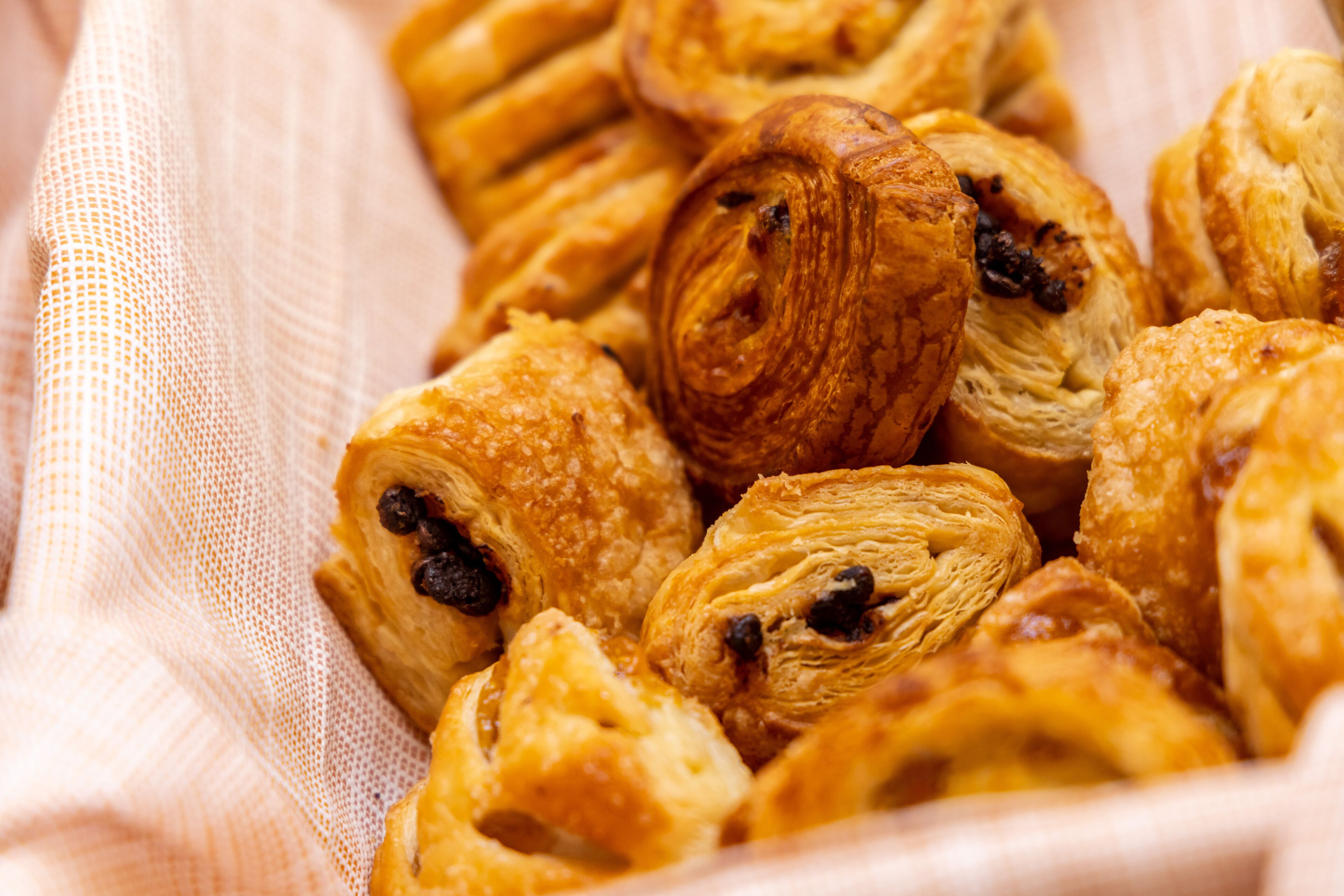 A basket of pastries, including croissants and puff pastries, on a cloth.