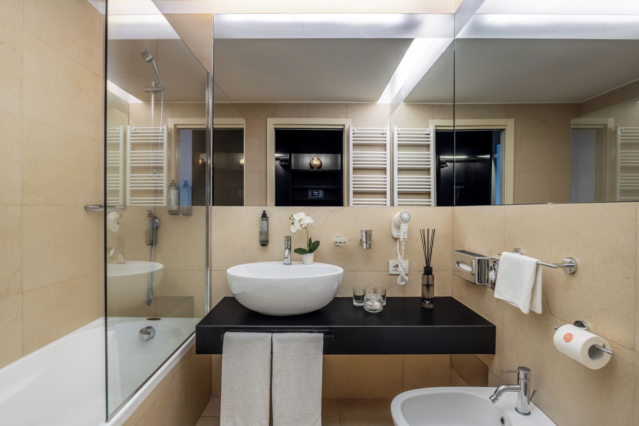 A modern bathroom with a large white sink, a black countertop, a glass-enclosed shower, and a bidet.