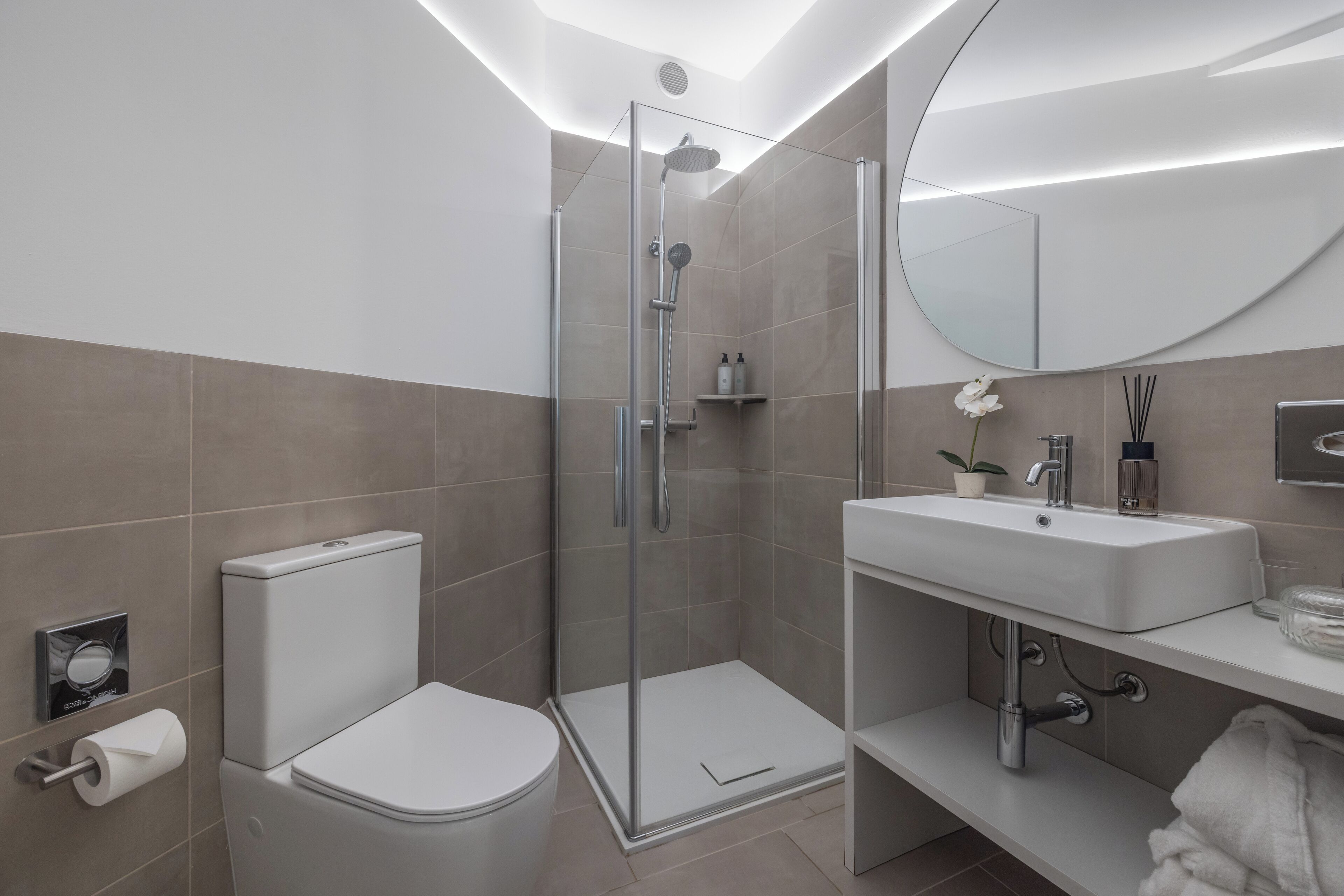 Un baño moderno con ducha de vidrio, inodoro, lavamanos y espejo.