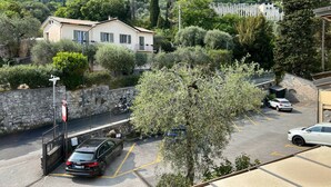 A residential area with a stone wall, parked cars, and houses surrounded by greenery. - Hotel Meandro - Lake View (Gargnano)
