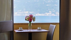 A table with a vase of flowers and two cups, overlooking a scenic view. - Hotel Meandro - Lake View (Gargnano)