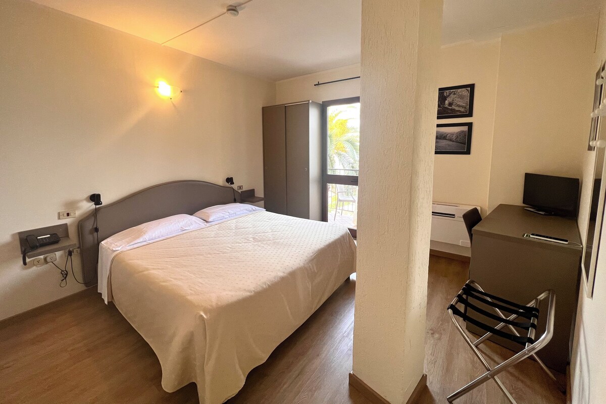 Habitación de hotel con cama, mesita de noche, lámpara, escritorio con silla y televisor.