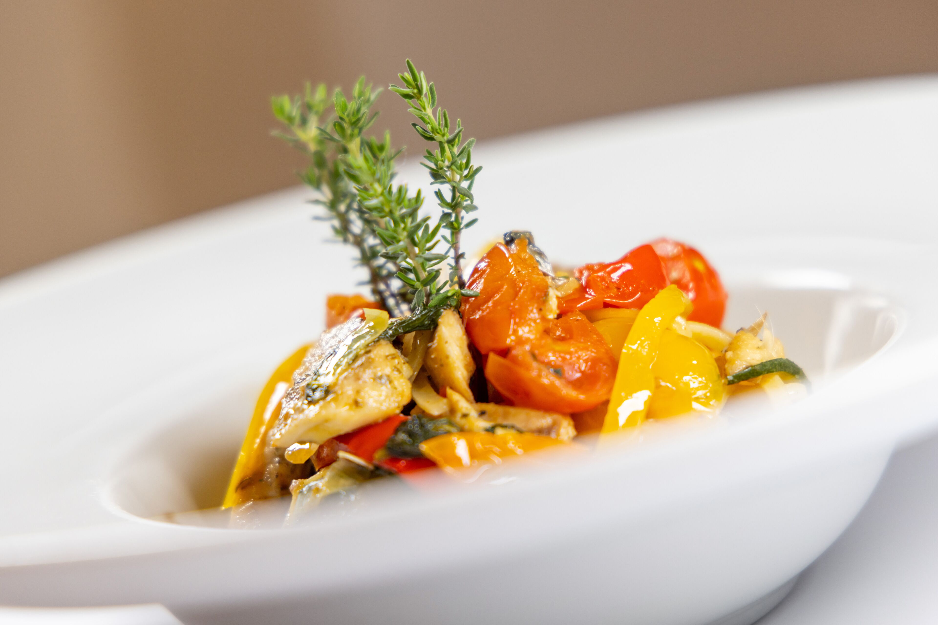 A white plate with a dish of roasted vegetables and a sprig of thyme.