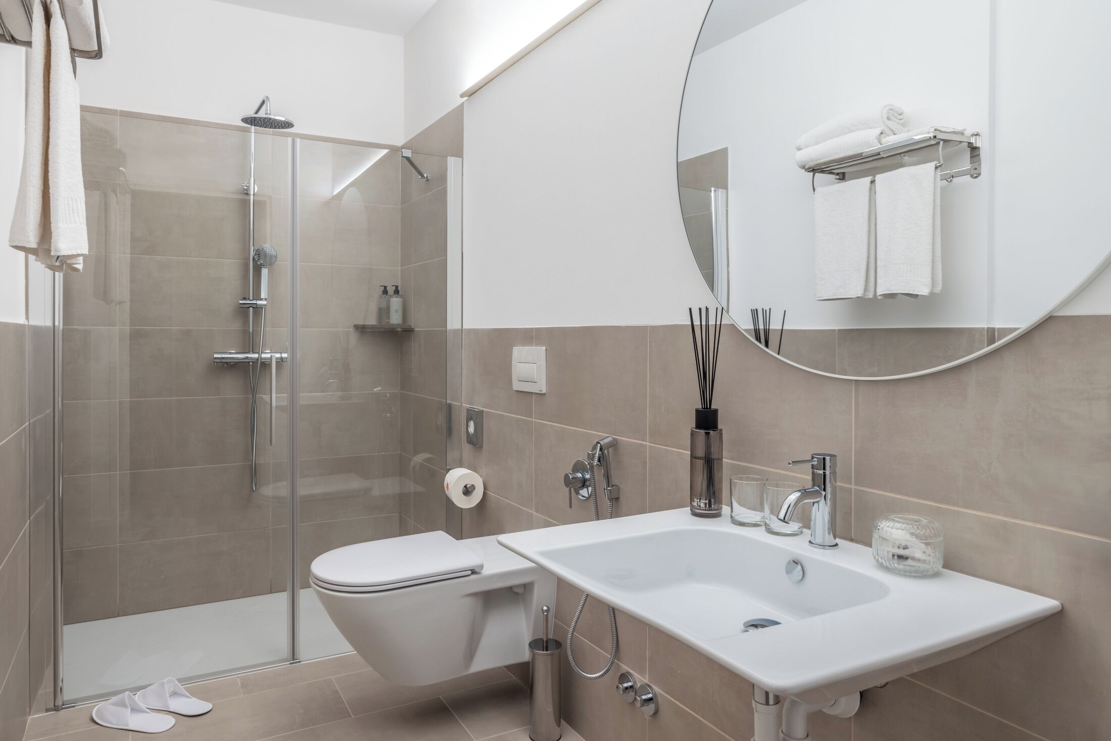 Een moderne badkamer met een douche met glazen wand, een wit toilet, een wastafel met spiegel en een handdoekhouder.