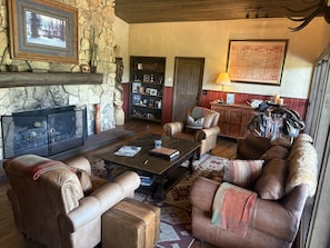 A cozy living room with leather sofas, a fireplace, a bookshelf, and a map on the wall.