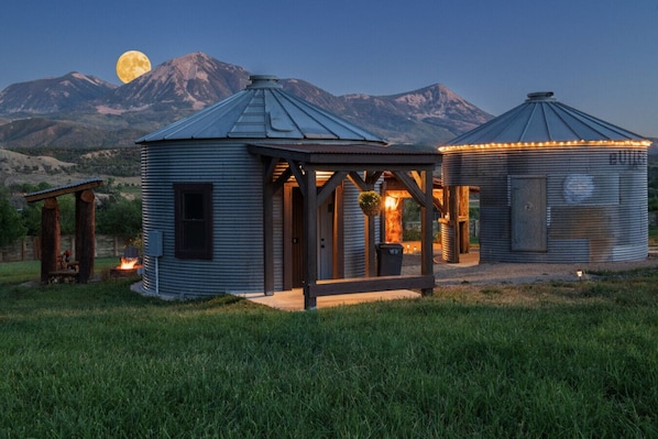 A rustic cabin with a metal roof, a wooden porch, and a small fire pit.
