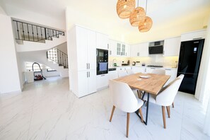Een moderne keuken met witte kasten, een houten eettafel en een trap.