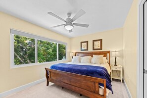 A bedroom with a large window, a ceiling fan, a wooden bed, and two bedside tables. - Go to the beach from expansive heated pool home (Fort Myers Beach)