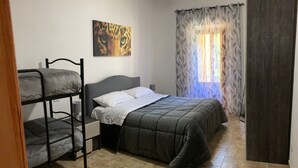 A room with bunk beds, a single bed, a painting on the wall, and a window with patterned curtains. - Apartment with terrace and garden  (Borgo Cerreto)