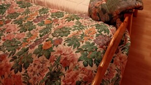 Ein Schlafzimmer mit zwei Einzelbetten, Holz-Kopfteilen, floralen Bettdecken und einem Fenster mit gemusterten Vorhängen.