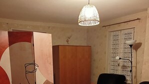 Ein Wohnzimmer mit Holzboden, einem Holzkasten, einem schwarzen Sessel mit roten Kissen, einem kleinen Holztisch und einer Pendelleuchte.