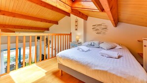 Un dormitorio con techo de madera, una cama con ropa de cama blanca, una mesita de noche y un estante montado en la pared.