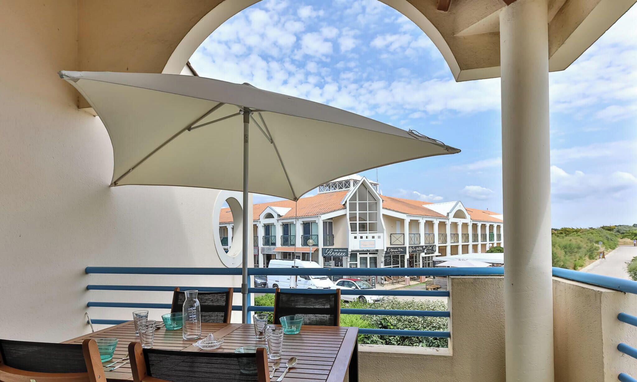 A balcony with a table, chairs, and a large umbrella. There is a view of a building with multiple windows and a red roof.