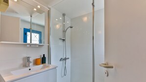 Un baño moderno con cabina de ducha de vidrio, un lavabo blanco con espejo arriba y una puerta azul al fondo.