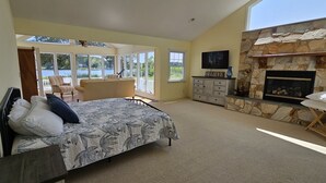A bedroom with a bed, a fireplace, a TV, and a view of a lake.