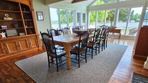 A dining area with a wooden table and chairs, a built-in wooden cabinet, and large windows offering a view of the outdoors.