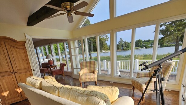 A spacious room with a large window overlooking a lake, a ceiling fan, a sofa, and a telescope.