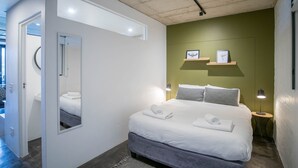 Een moderne hotelkamer met een groot bed, een spiegel, een nachtkastje met een lamp en kunst aan de muur.