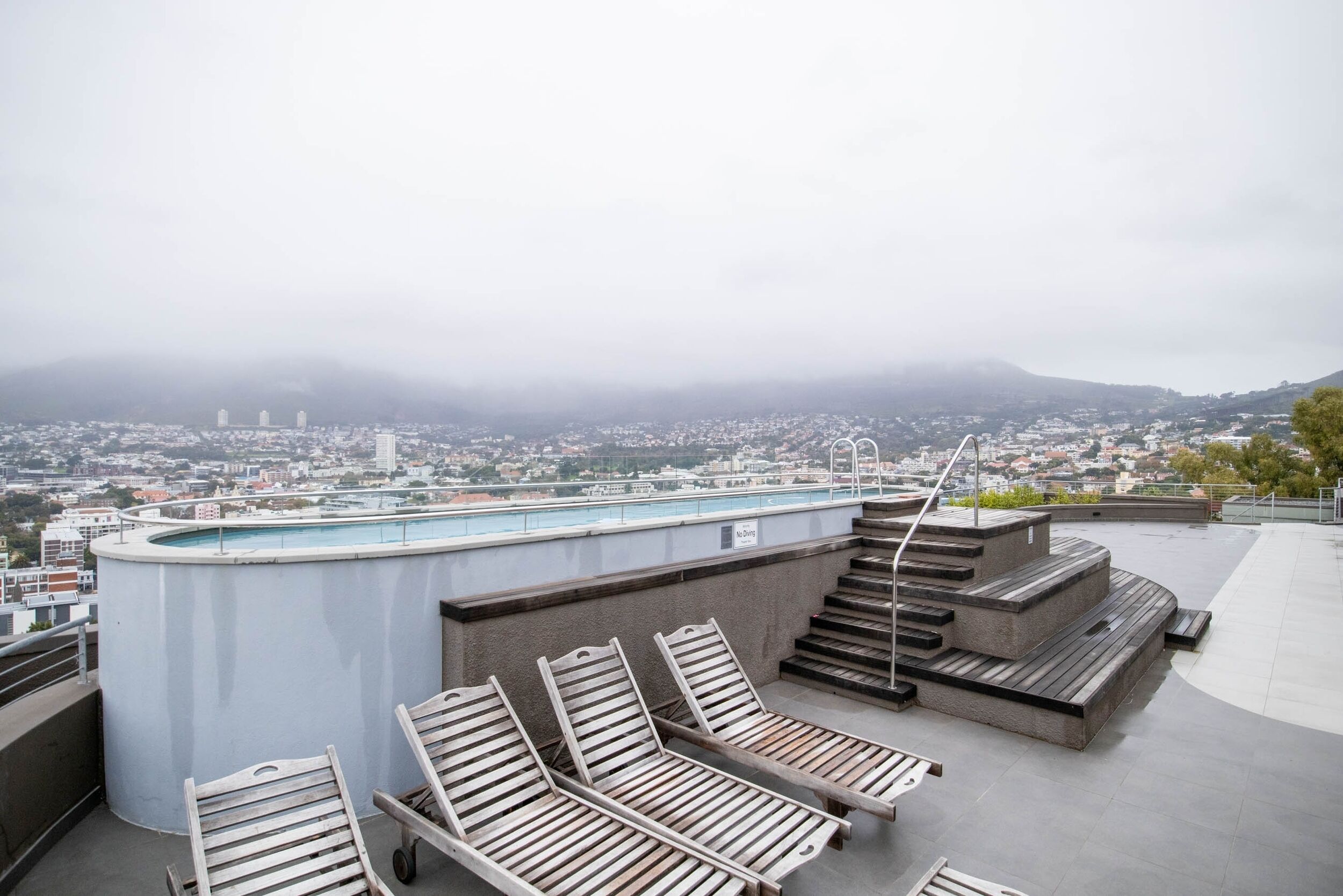 A rooftop terrace with a pool, lounge chairs, and a view of a cityscape.