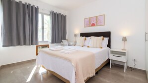 A bedroom with a bed, bedside tables, a desk, and a window with curtains. - Local 102 Apartment  (Rio de Janeiro)