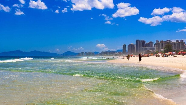 A beach with clear waters, a sandy shore, and a cityscape in the background. - Local 102 Apartment  (Rio de Janeiro)