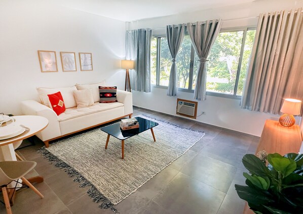A modern living room with a white sofa, a round coffee table, and a large window with curtains.