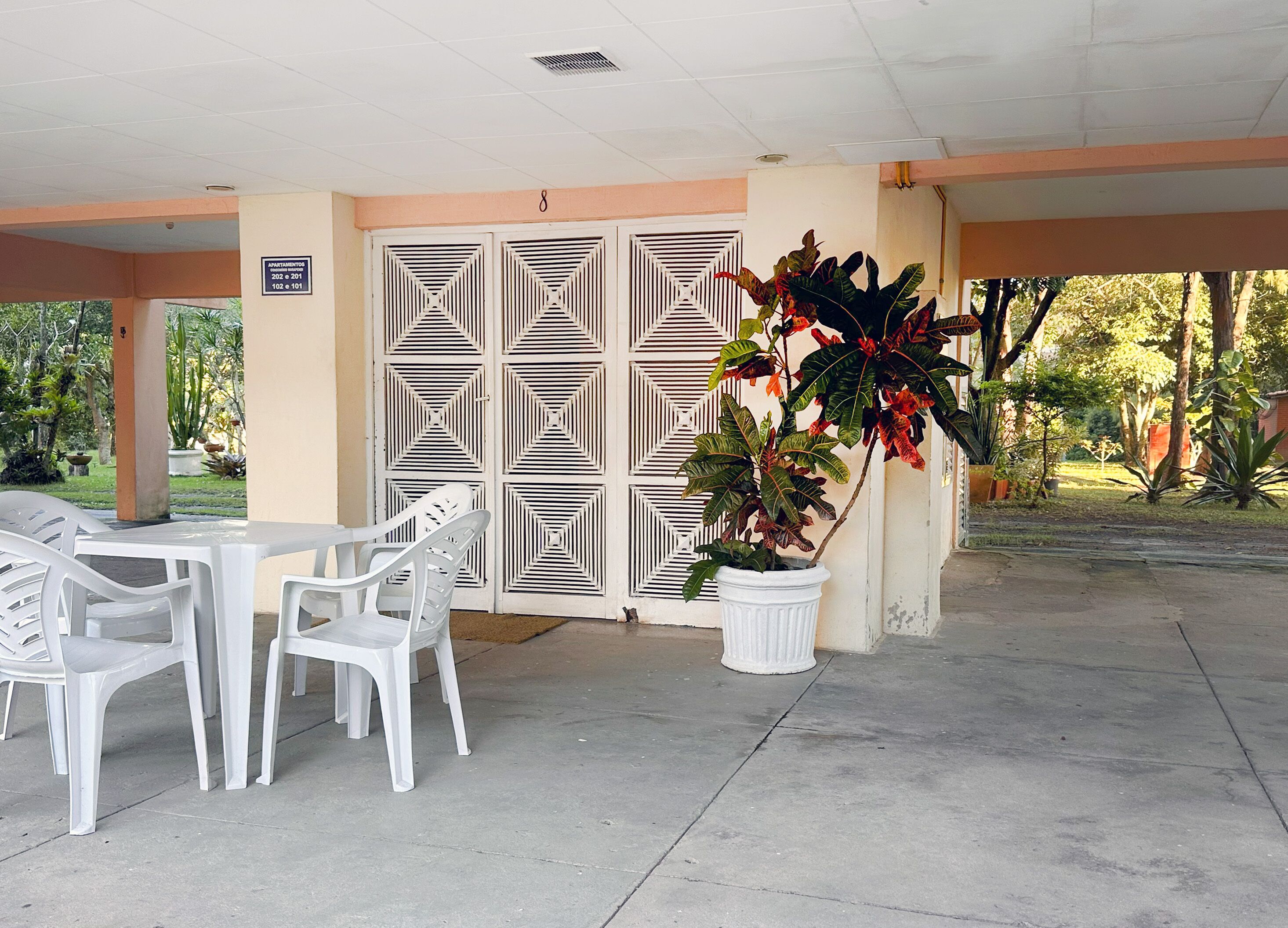 A covered outdoor seating area with white plastic chairs and a potted plant.