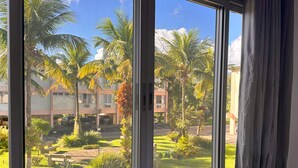 A room with a large window overlooking a courtyard with palm trees and a building in the background. - Local 102 Apartment  (Rio de Janeiro)