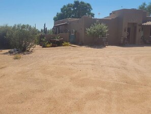 Set amidst sparse desert vegetation, this property features a stucco exterior and a large, open driveway leading to the entrance.