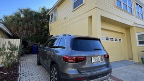 A two-story house with a garage, a parked SUV, and a paved driveway. - Florida Beachfront Bliss just steps from the Sand (St. Pete Beach)