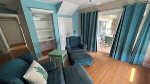 A living room with teal walls, a ceiling fan, a wooden floor, and a view of an outdoor patio with a table and chairs. - Florida Beachfront Bliss just steps from the Sand (St. Pete Beach)