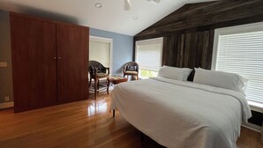 A bedroom with a bed, wooden wardrobe, two chairs, a ceiling fan, and large windows with blinds. - Florida Beachfront Bliss just steps from the Sand (St. Pete Beach)