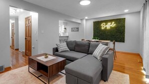 A modern living room with a grey sectional sofa, a wooden coffee table, and a neon sign on the wall. - Modern Trendy Downtown (Buffalo)