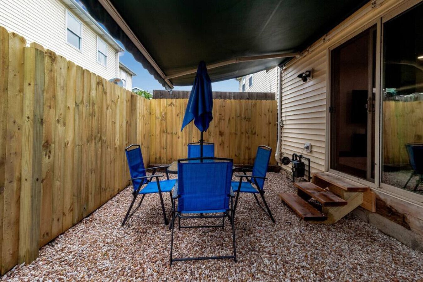 Un patio techado con una mesa y sillas, cerca de madera y suelo de grava.