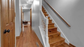 A hallway with wooden flooring and white walls, leading to a staircase with wooden steps and white railings. - Modern Trendy Downtown (Buffalo)