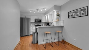 A modern kitchen with white cabinets, stainless steel appliances, and a wooden floor. - Modern Trendy Downtown (Buffalo)