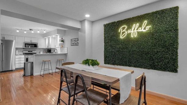 A modern kitchen with white cabinets, stainless steel appliances, and a dining area with a wooden table and chairs. - Modern Trendy Downtown (Buffalo)