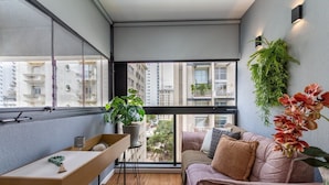 Un apartamento moderno con un ventanal grande, un escritorio de madera, un sofá rosa y una planta verde.