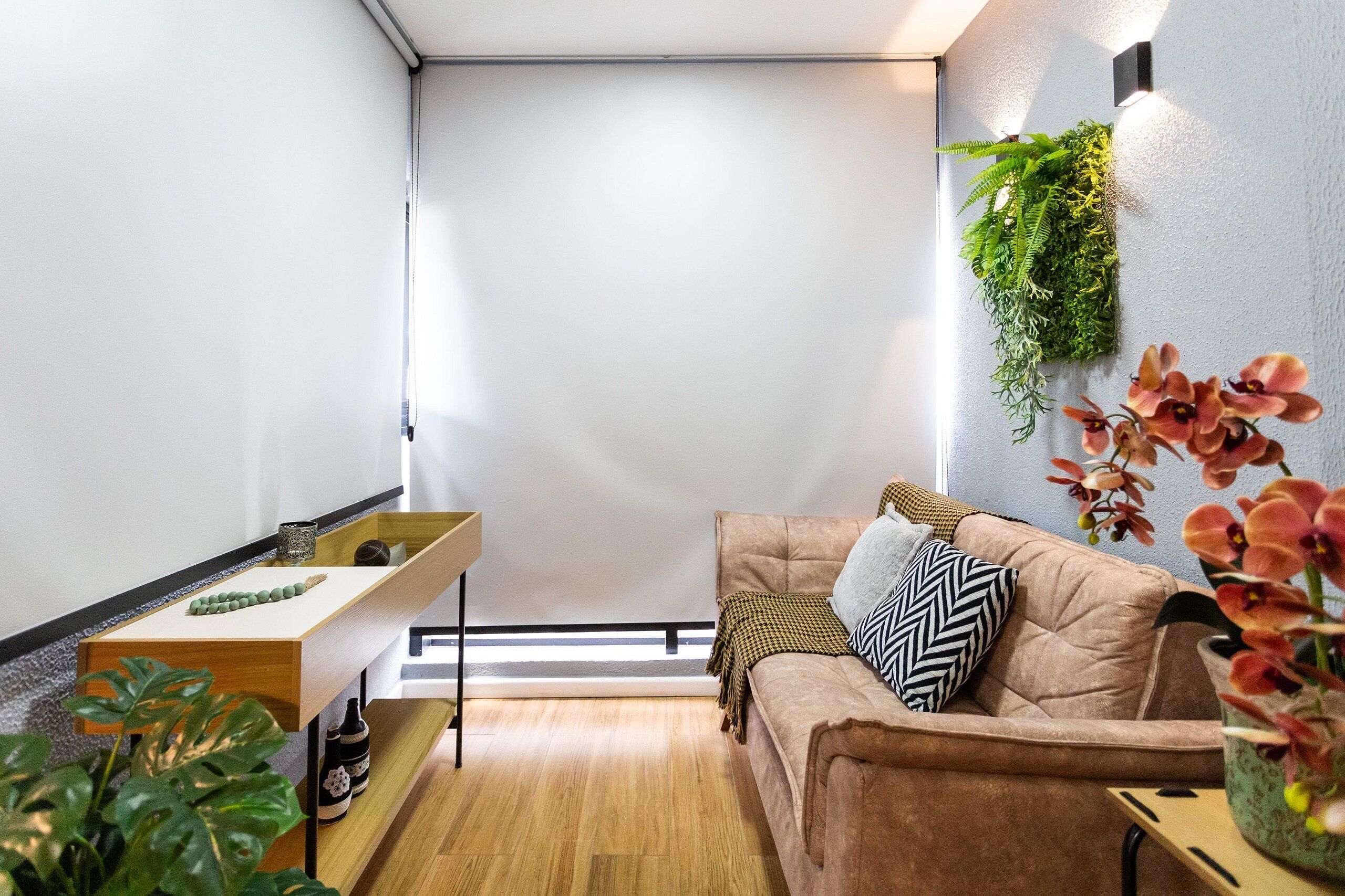 Un salon moderne avec un plancher en bois, un canapé marron agrémenté de coussins à motifs, une petite table d’appoint en bois et une plante fixée au mur.