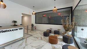 Un área de recepción moderna con suelo de mármol, una mesa de recepción y asientos con mesitas redondas y pufs.