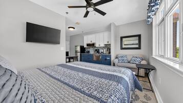 A bedroom with a bed, a ceiling fan, a TV, a kitchenette, and a window.