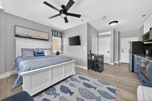 A bedroom with a bed, ceiling fan, TV, and a view of the kitchen. - #2400 Pointe - Studio Suite at Mariners SML (Huddleston)