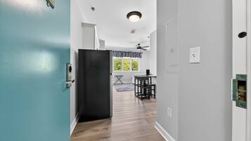 Un couloir avec une porte de couleur turquoise, un réfrigérateur noir, un coin repas avec une table et des chaises, et un ventilateur de plafond.