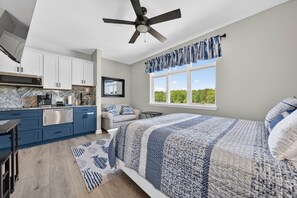 A bedroom with a bed, a window with a view, a ceiling fan, and a kitchen area. - #2400 Pointe - Studio Suite at Mariners SML (Huddleston)